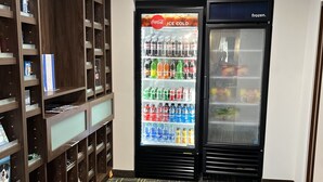 Um saguão de hotel com uma máquina de venda automática de Coca-Cola, um freezer e um escorredor de sapatos.