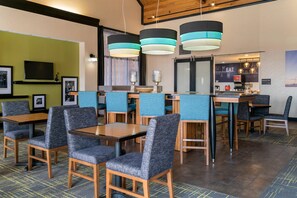 A modern restaurant with blue upholstered chairs, wooden tables, and pendant lighting. - Comfort Inn & Suites Toledo North (Toledo)