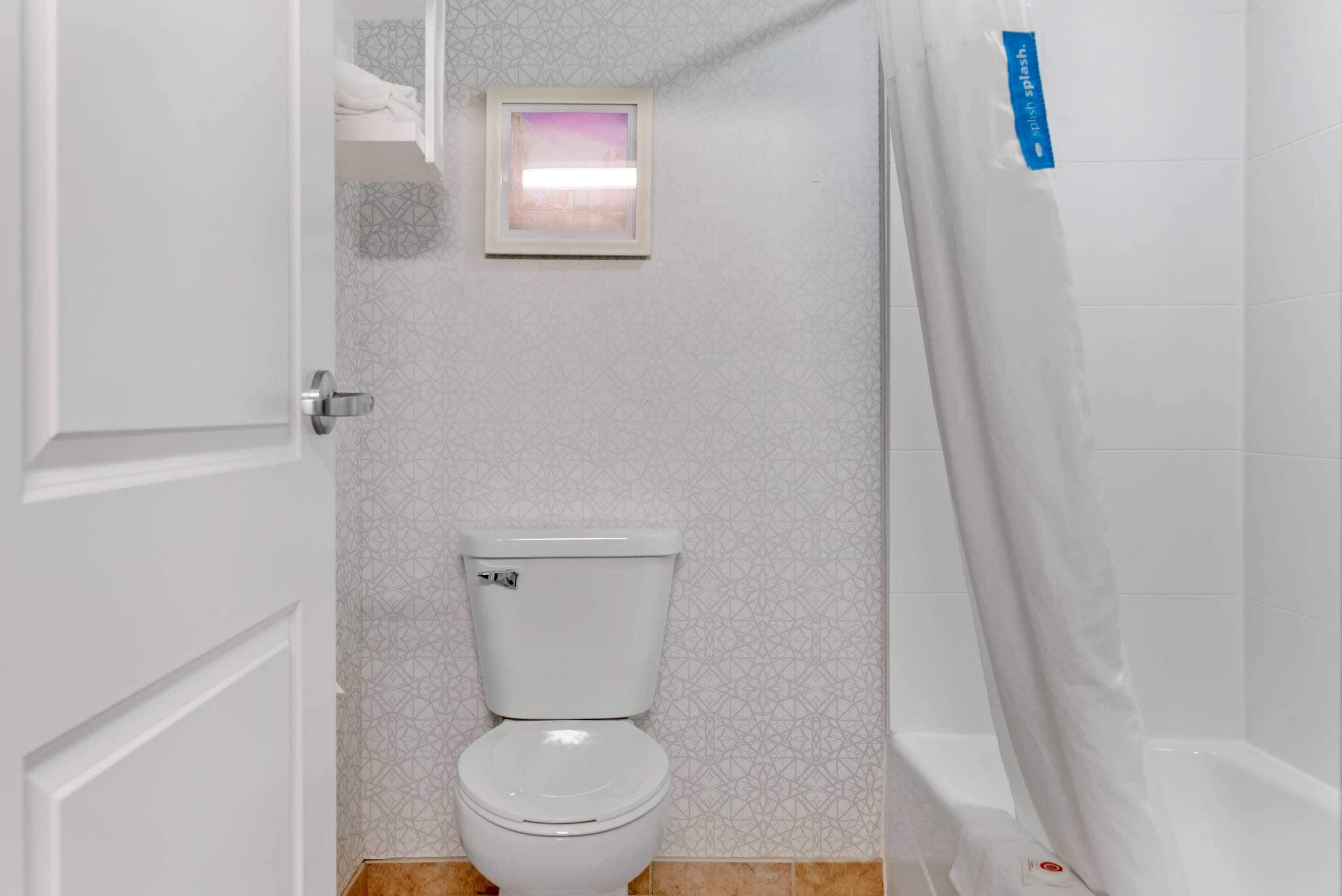 Een badkamer met een toilet, een douchegordijn en een ingelijst foto aan de muur.