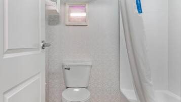 Een badkamer met een toilet, een douchegordijn en een ingelijst foto aan de muur.