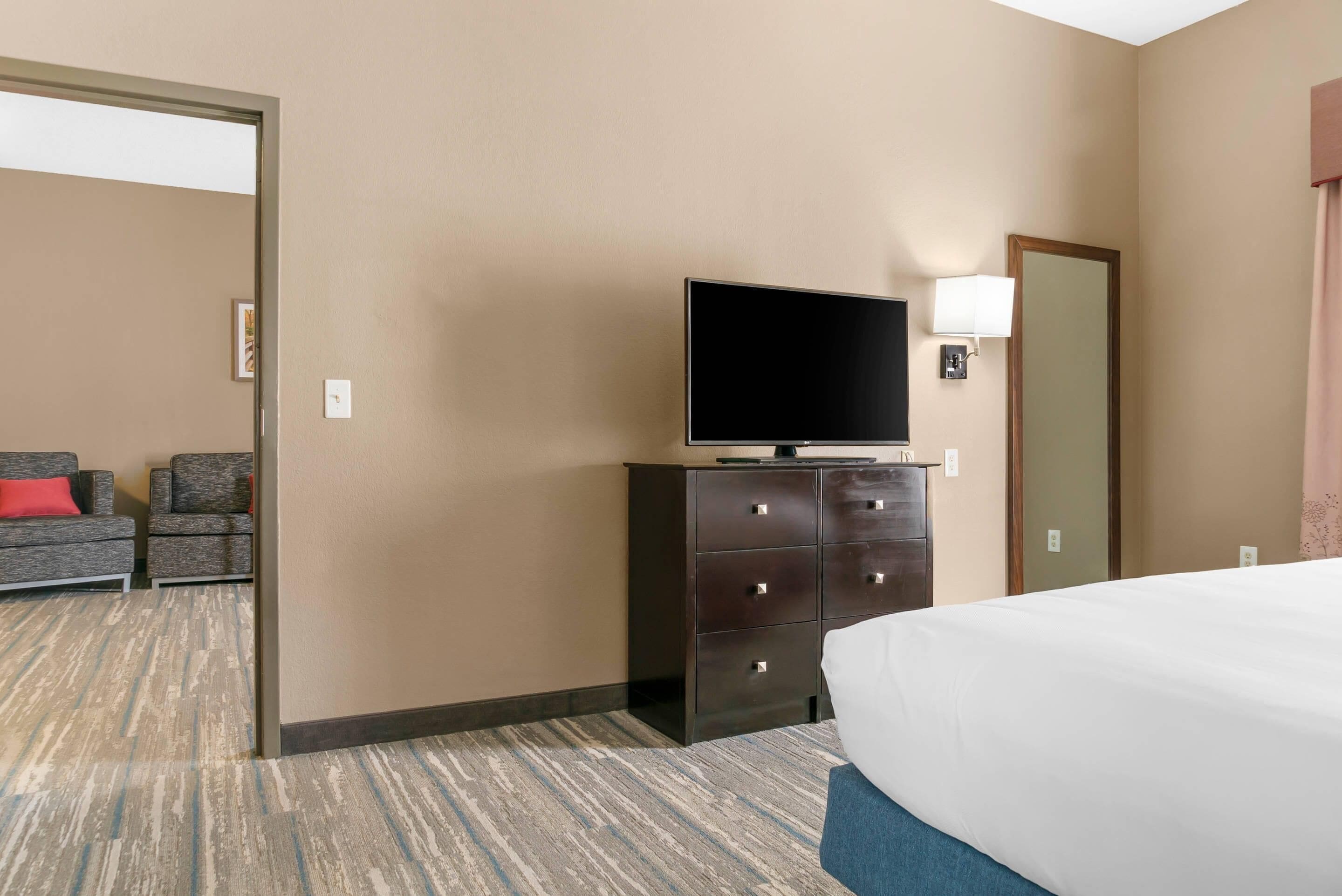 A hotel room with a bed, a television on a dresser, a chair, and a door.