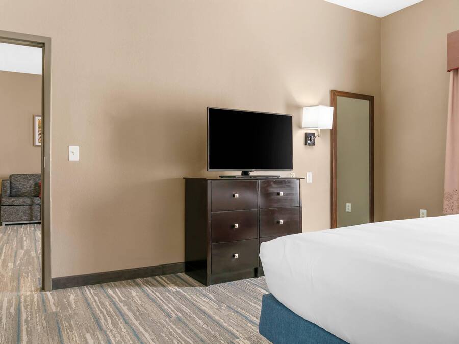 A hotel room with a bed, a television on a dresser, a chair, and a door.