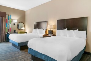 A hotel room with two beds, a nightstand with a lamp, a bedside table with a clock, and a wall-mounted mirror.