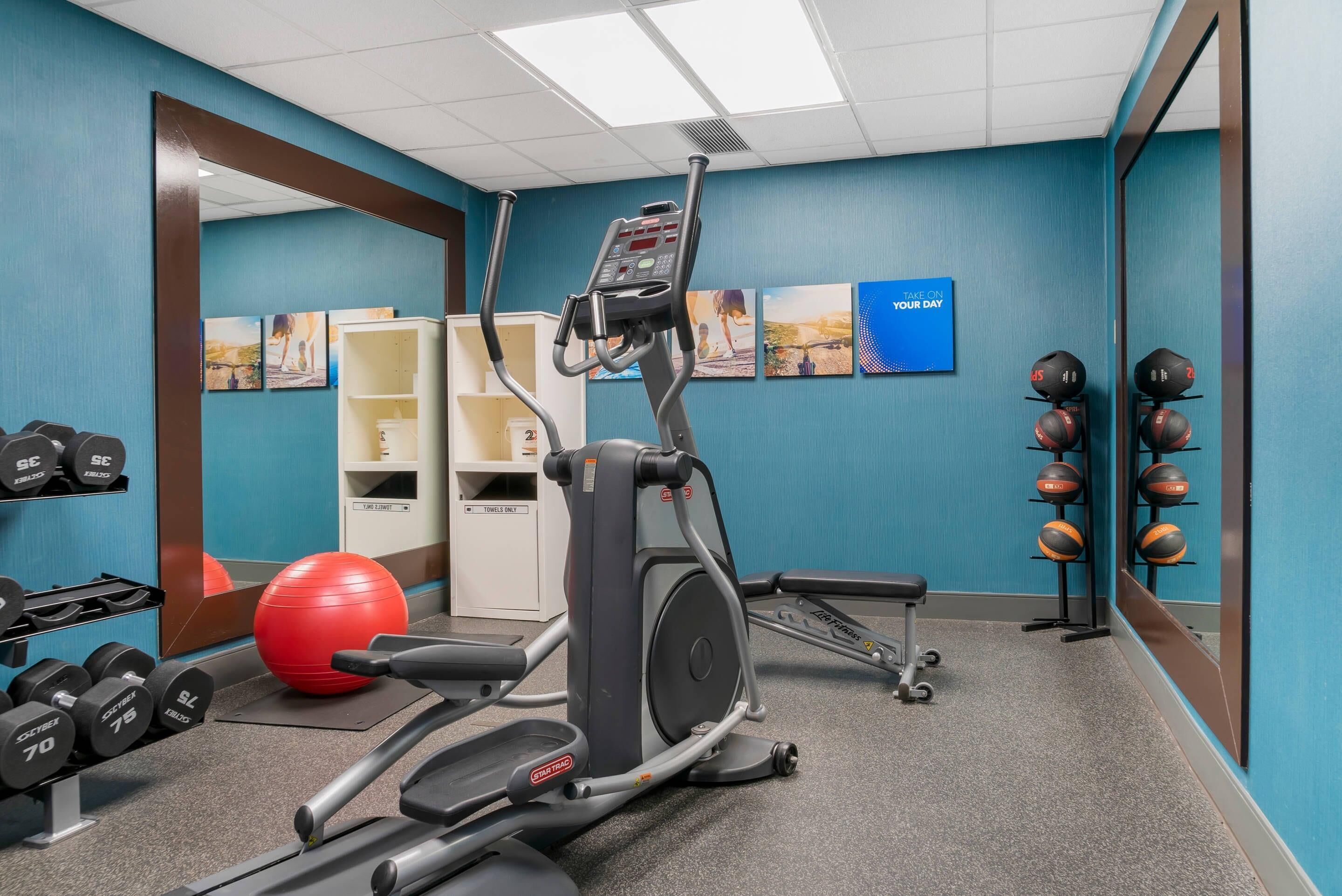 A gym with exercise equipment, a red exercise ball, dumbbells, and a wall with motivational posters.