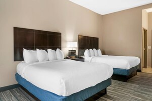 Habitación de hotel con dos camas, una mesita de noche con lámpara y una puerta a la derecha.