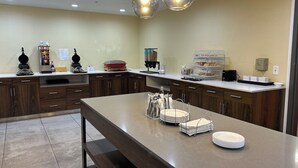 A modern kitchen with a central island, wooden cabinets, and a variety of appliances including a waffle maker and a coffee machine. - Comfort Inn & Suites Toledo North (Toledo)