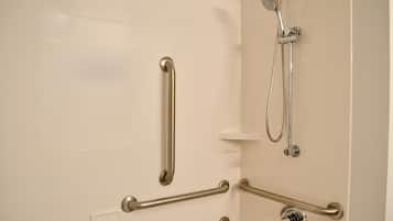 A bathroom with white tiled walls, a shower with a handheld showerhead, and multiple grab bars for support.