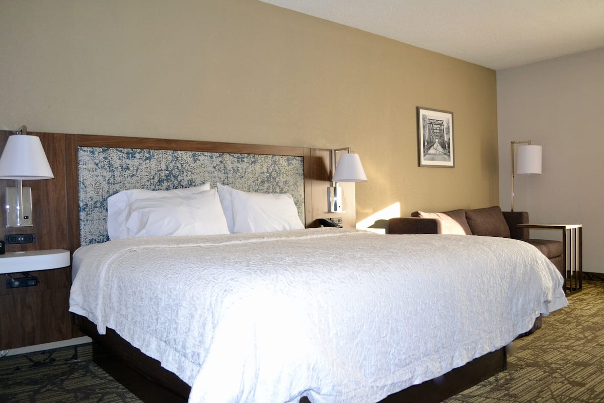 A hotel room with a large bed, two bedside tables, a nightstand, a chair, and a framed picture on the wall.