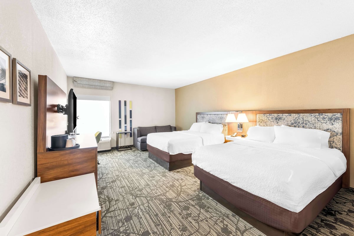 A hotel room with two beds, a desk, a chair, a TV, and a window.