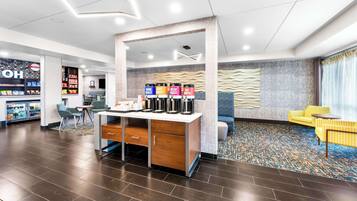 A modern hotel lobby with a coffee station, seating area, and a snack bar.