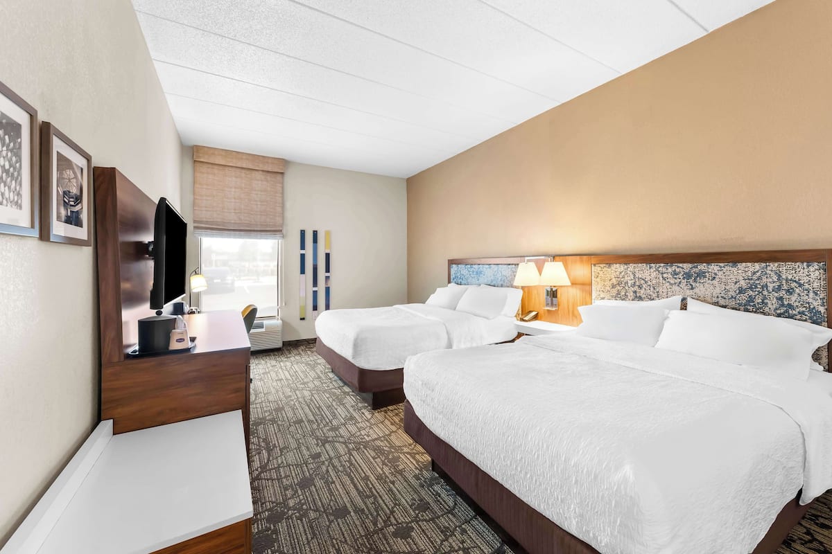 A hotel room with two beds, a desk, a TV, and a window with a view.