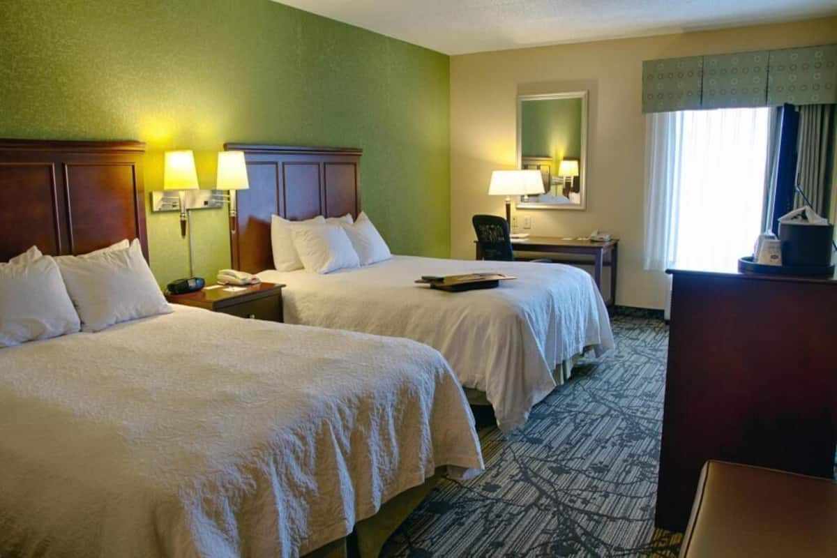A hotel room with two beds, a desk, a chair, and a window with curtains.