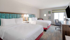 Ein Hotelzimmer mit zwei Betten, einem Schreibtisch, einem Stuhl und einem Fernseher.