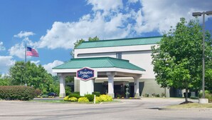 A Hampton Inn with a green roof, American flag, and a signboard.