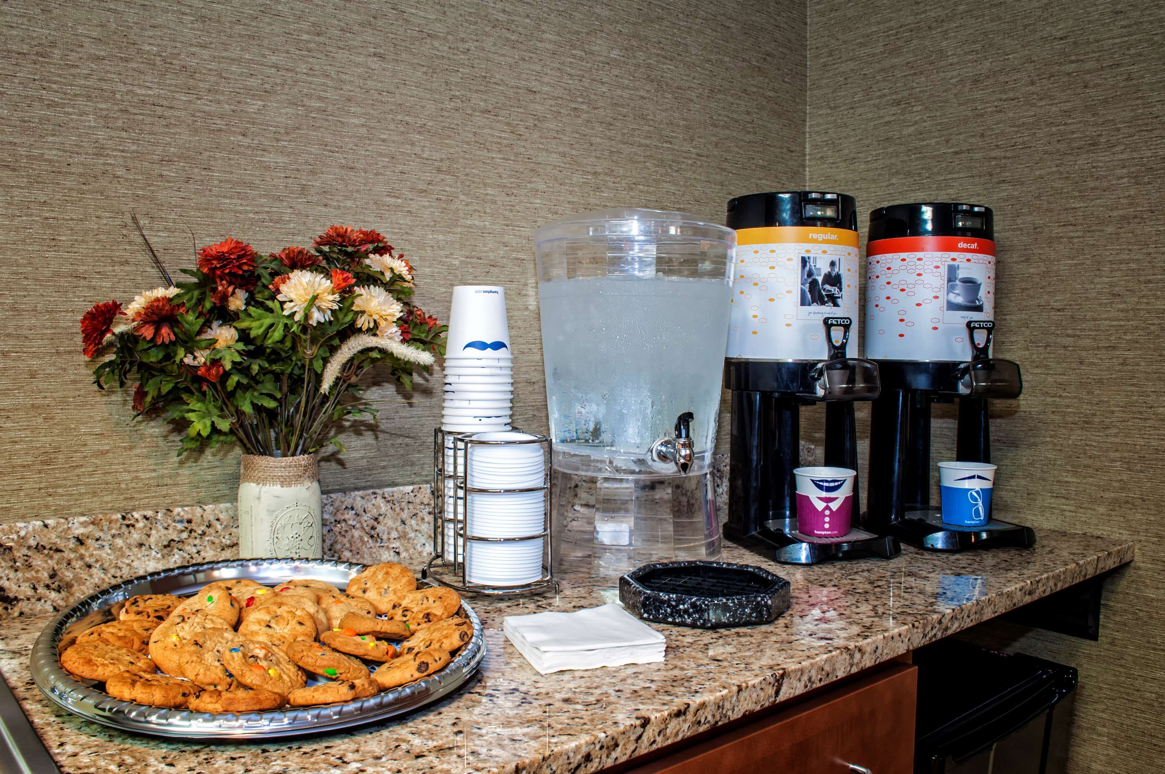 A kitchen counter with a water dispenser, coffee makers, a plate of cookies, and a vase of flowers.