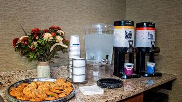 A kitchen counter with a water dispenser, coffee makers, a plate of cookies, and a vase of flowers.