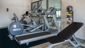 Ein Fitnessstudio mit Laufbändern, Crosstrainern und einer Bank.