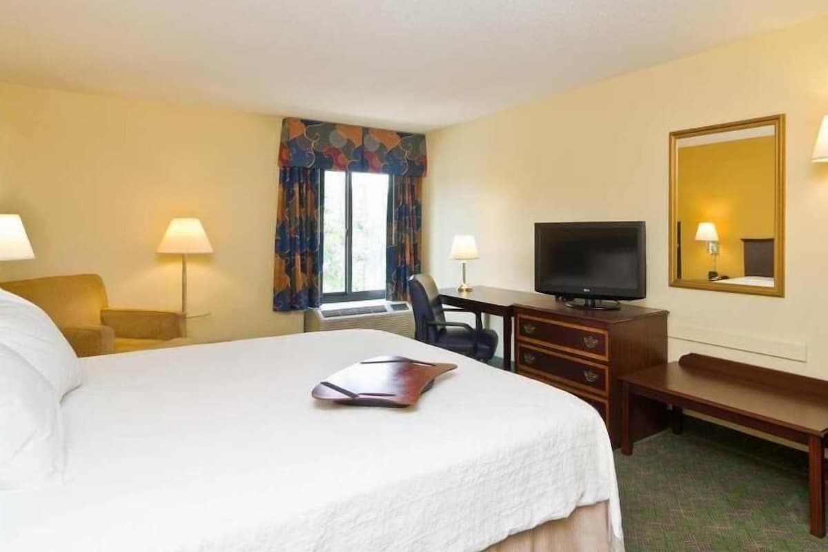 A hotel room with a bed, desk, chair, television, and a window with curtains.