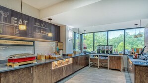 A modern kitchen with a breakfast bar, large windows, and a view of trees.