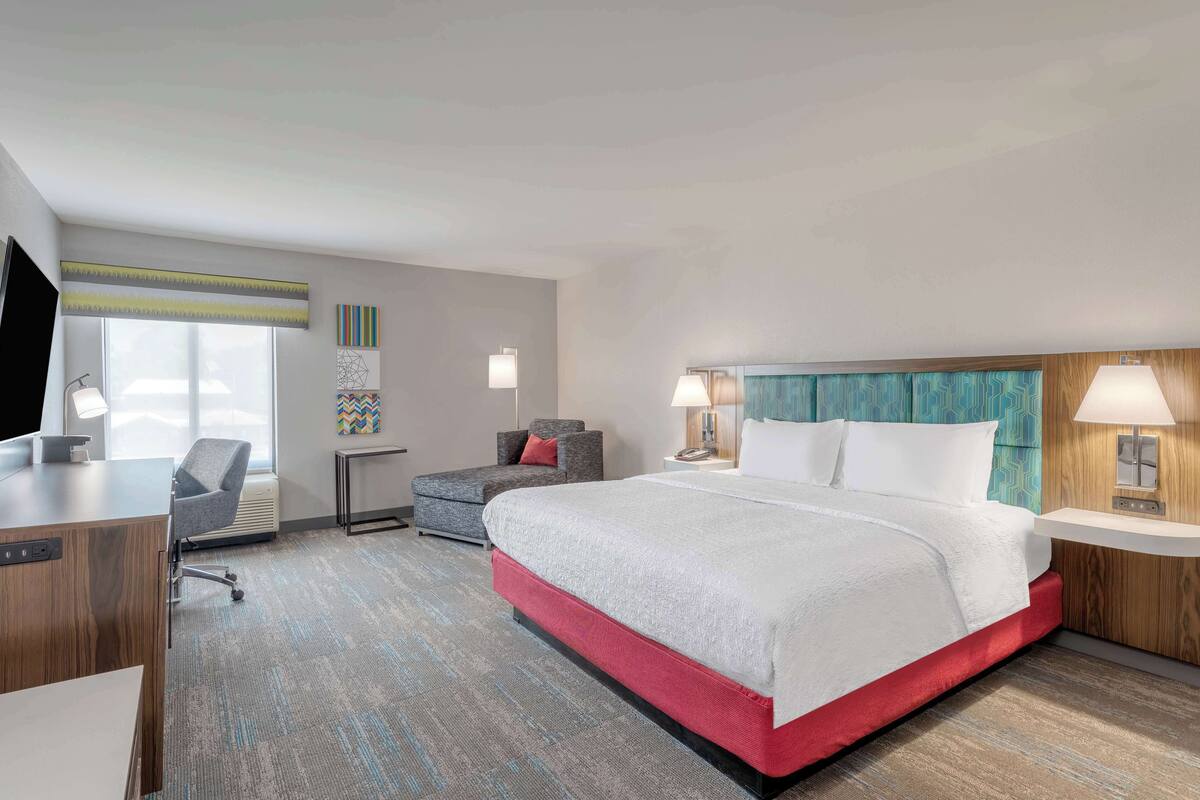 A hotel room with a large bed, a desk, a chair, and a TV.