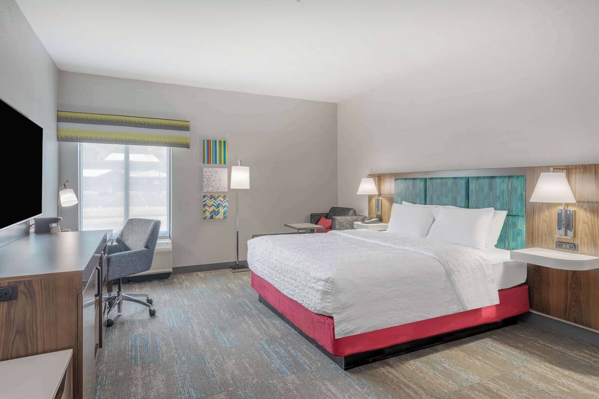 A hotel room with a bed, desk, chair, and a TV.