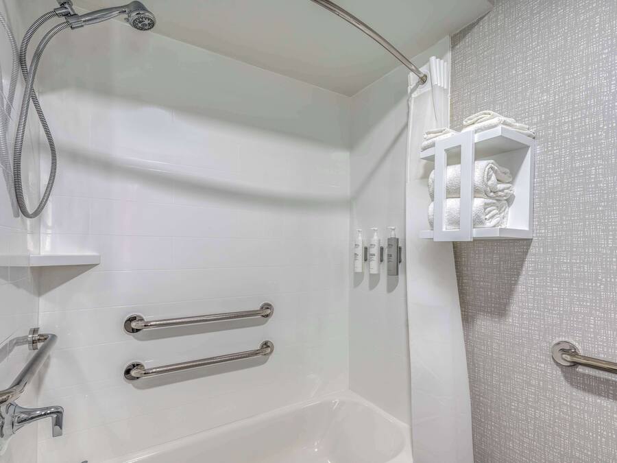 A modern bathroom with a bathtub, grab bars, a showerhead, and a towel rack.