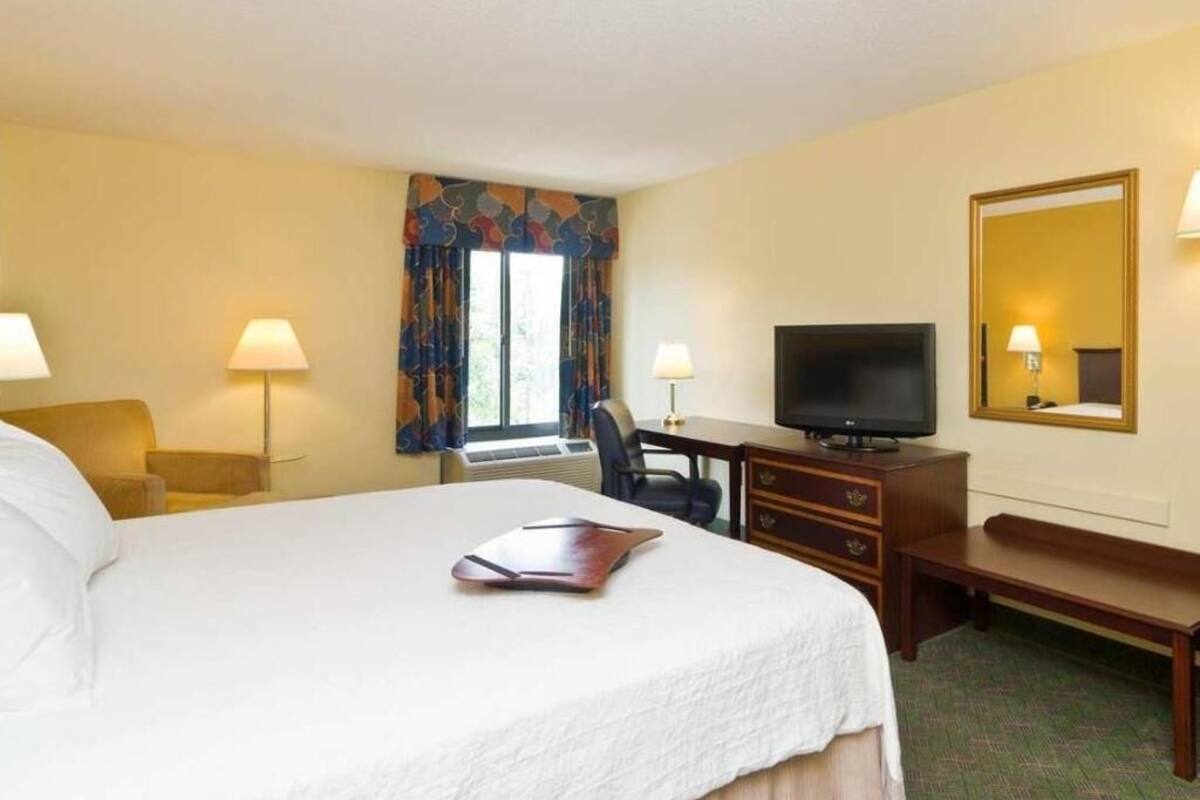 A hotel room with a bed, desk, television, and a mirror.