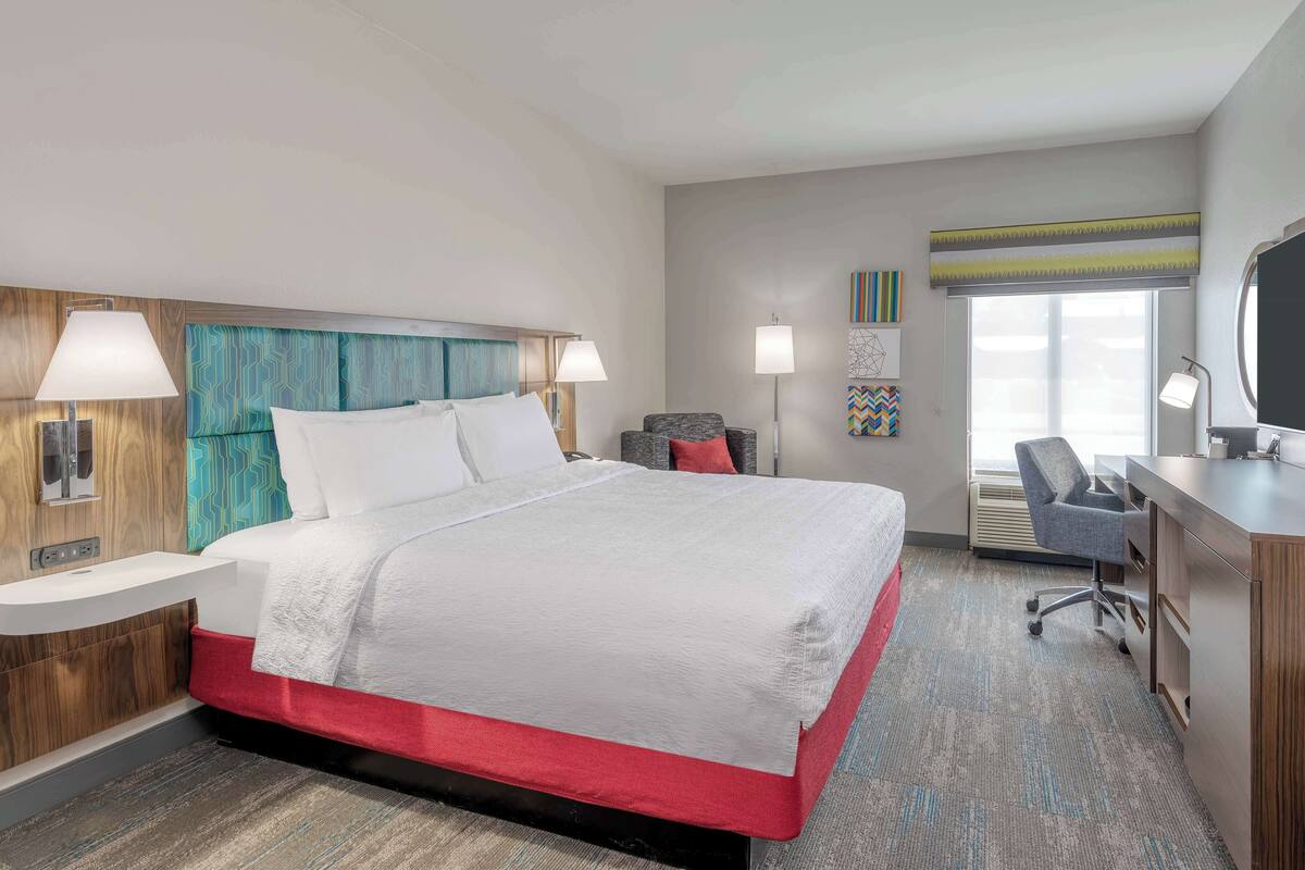 A modern hotel room with a large bed, a desk, and a chair.