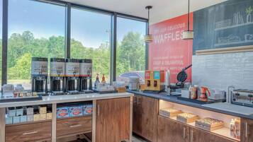 Une cuisine moderne équipée de machines à café, d’appareils à gaufres et de placards de rangement.
