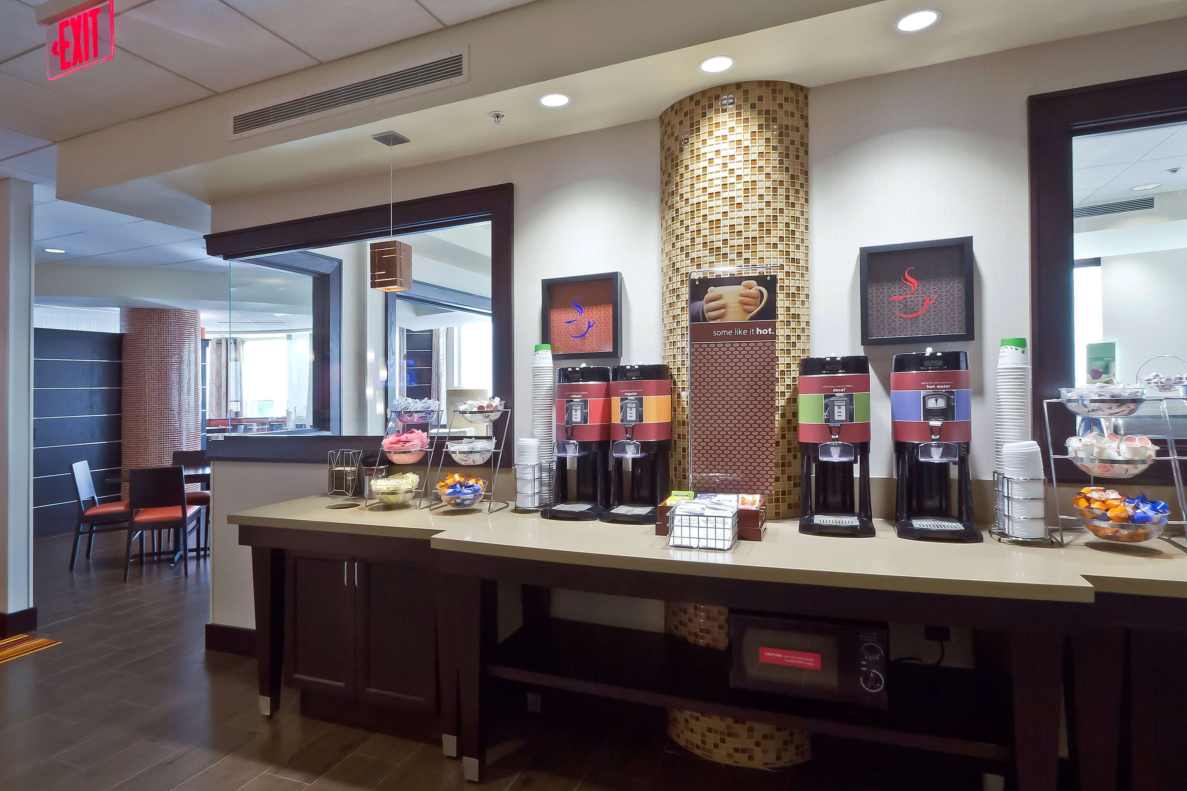 A hotel reception area with a coffee station, a framed artwork, and a display of coffee cups.