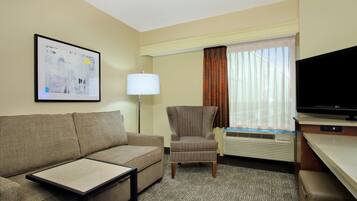 A hotel room with a sofa, armchair, flat-screen TV, and a framed picture on the wall.