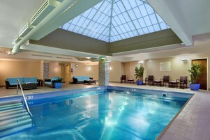 An indoor swimming pool with a skylight, lounge area with seating, and a clock on the wall.