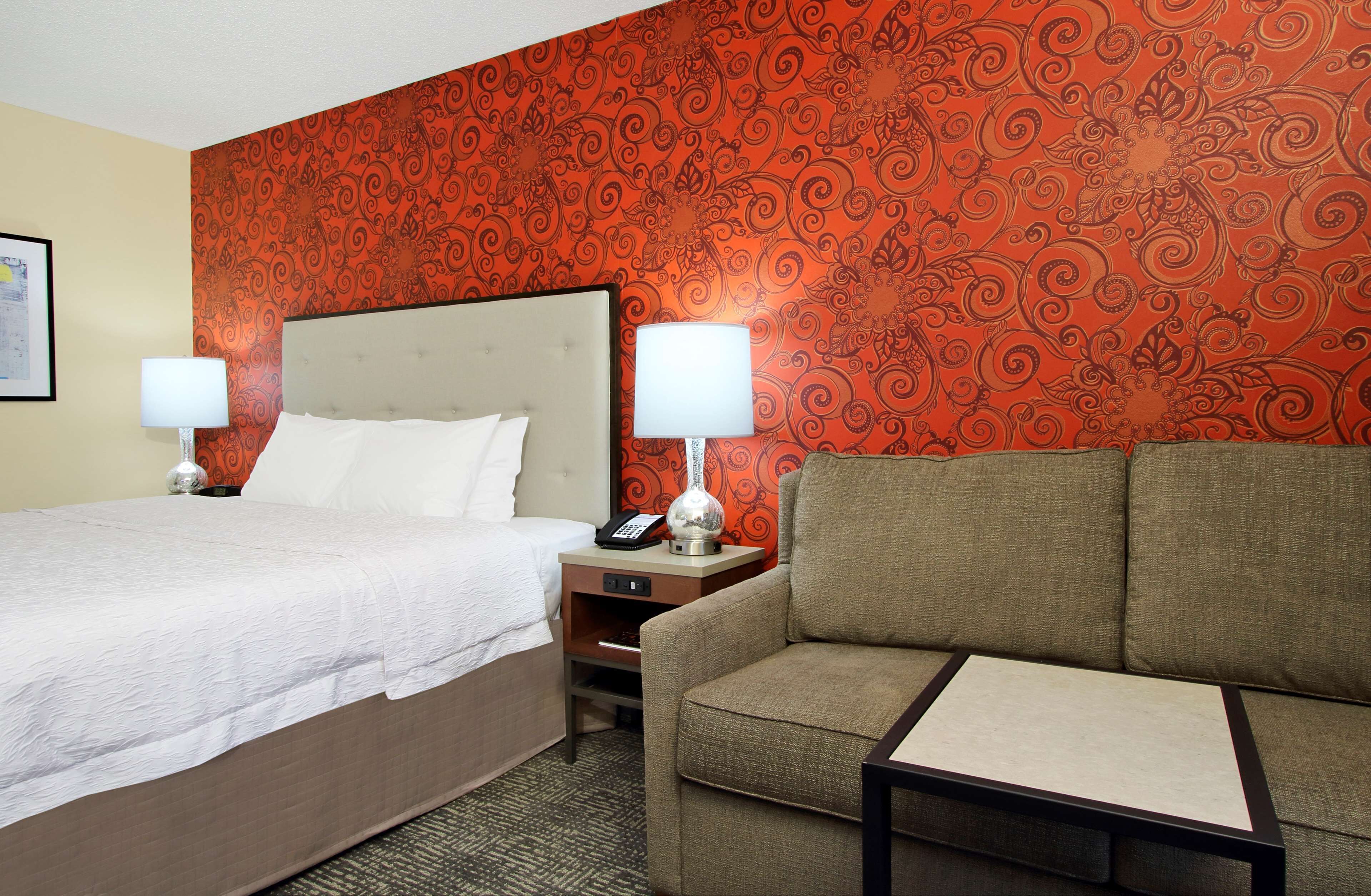A hotel room with a bed, a sofa, two bedside lamps, a nightstand, and a patterned wallpaper.