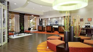 Eine moderne Hotelhalle mit Empfangstresen, Sitzgelegenheiten und großen Fenstern.