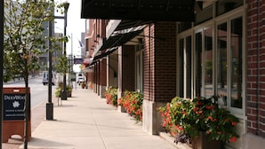 Ein Backsteinhaus mit großen Fenstern und einem Bürgersteig, der mit Pflanzgefäßen gesäumt ist.