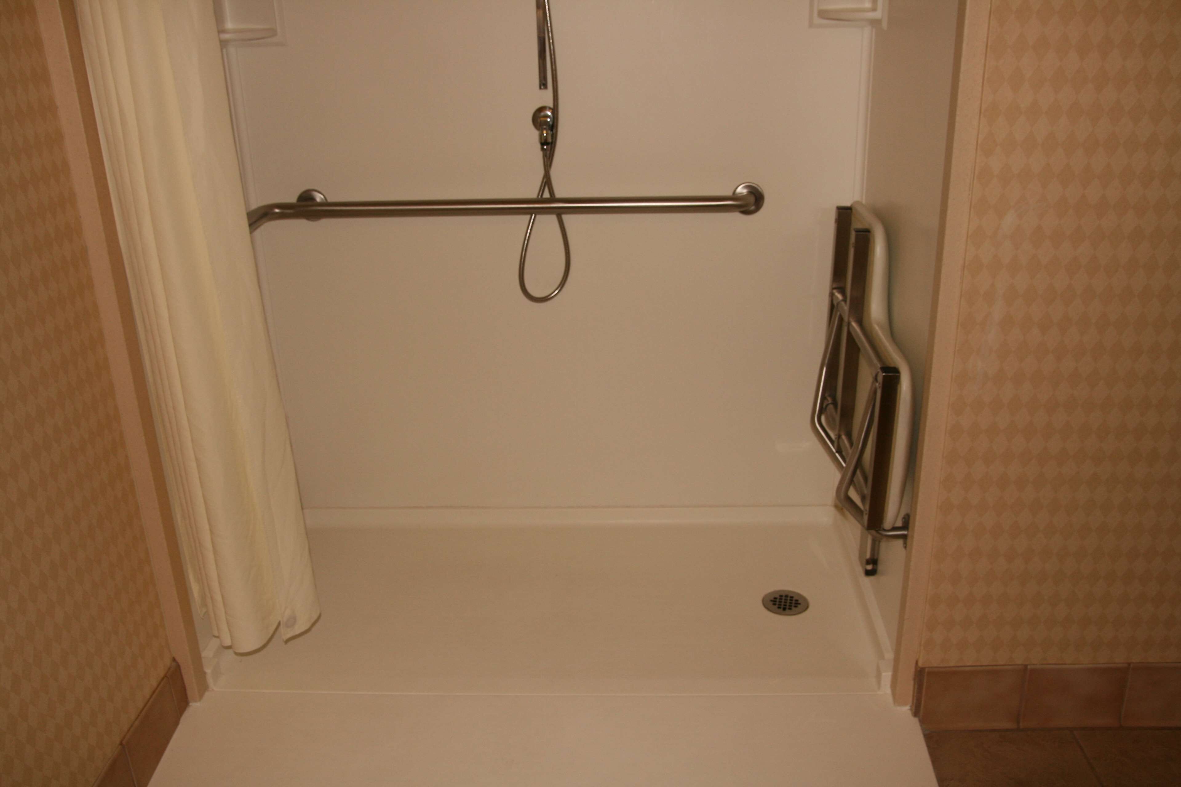 A bathroom with a shower area, a grab bar, and a handrail.