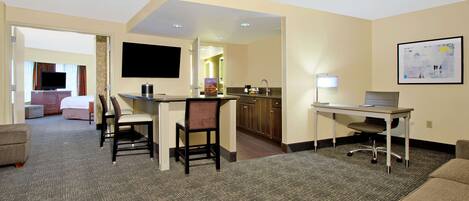 A hotel room with a kitchenette, a dining area, a TV, and a bed.
