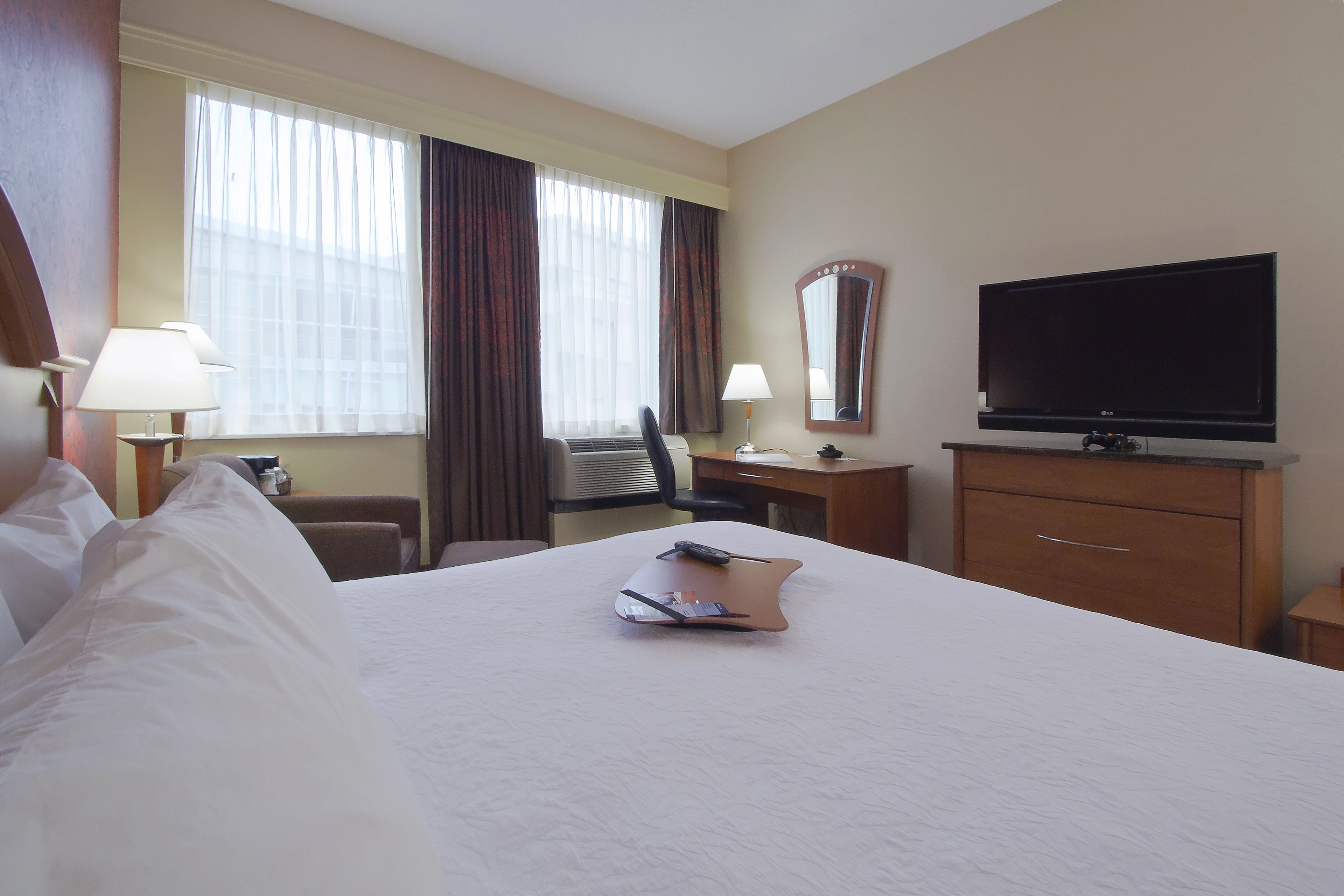 A hotel room with a large bed, a flat-screen TV, a desk with a chair, and a window with curtains.