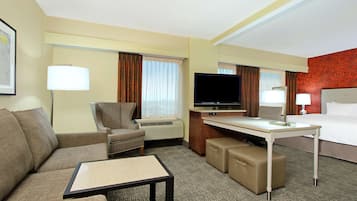 A hotel room with a sofa, armchair, desk, television, and a bed.