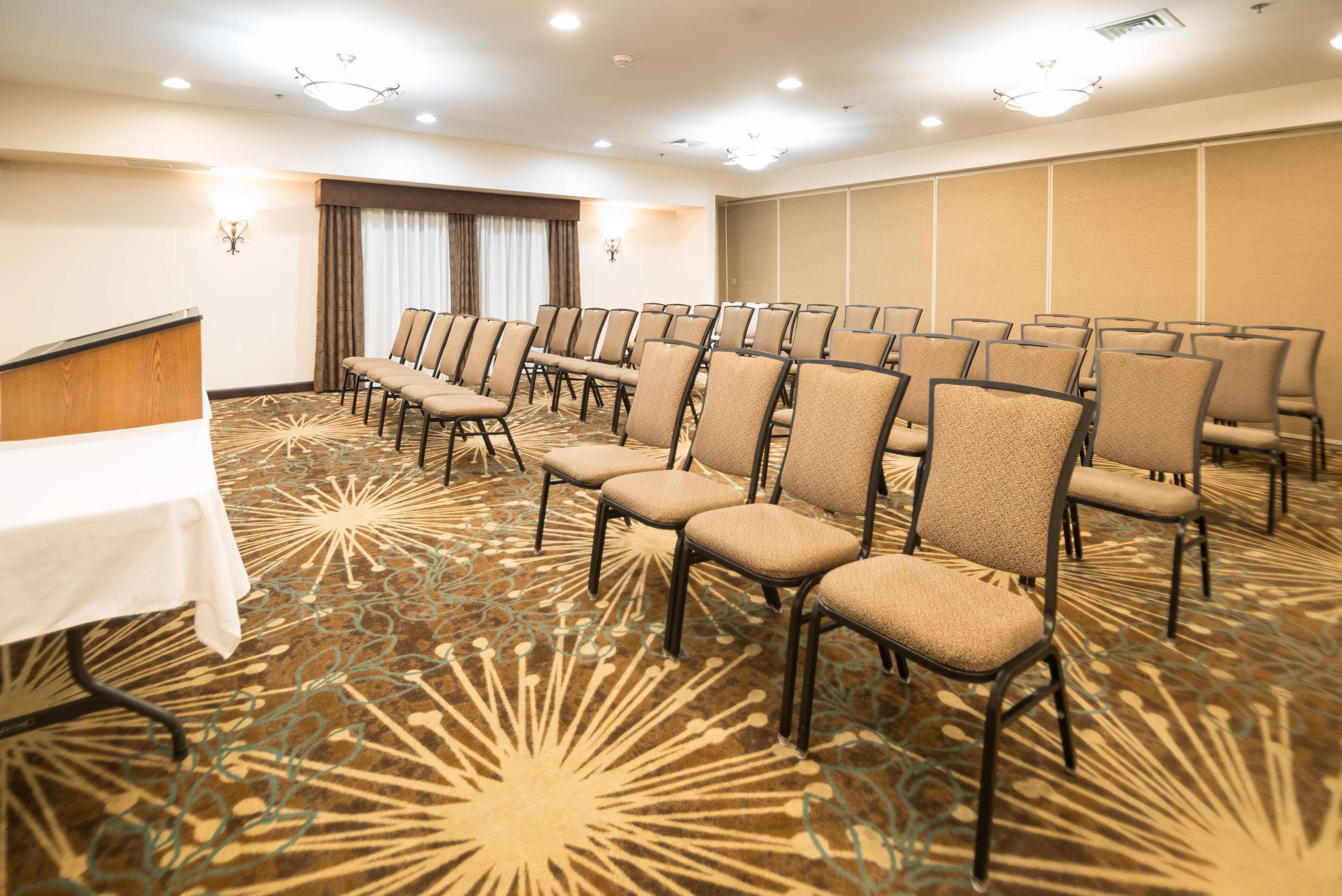 A conference room with rows of chairs, a table, and a patterned carpet.