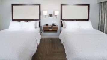 A hotel room with two beds, a nightstand, a lamp, and a wall-mounted light fixture.