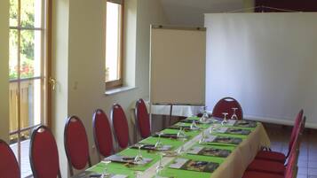 A conference room with a long table, red chairs, and a white screen.