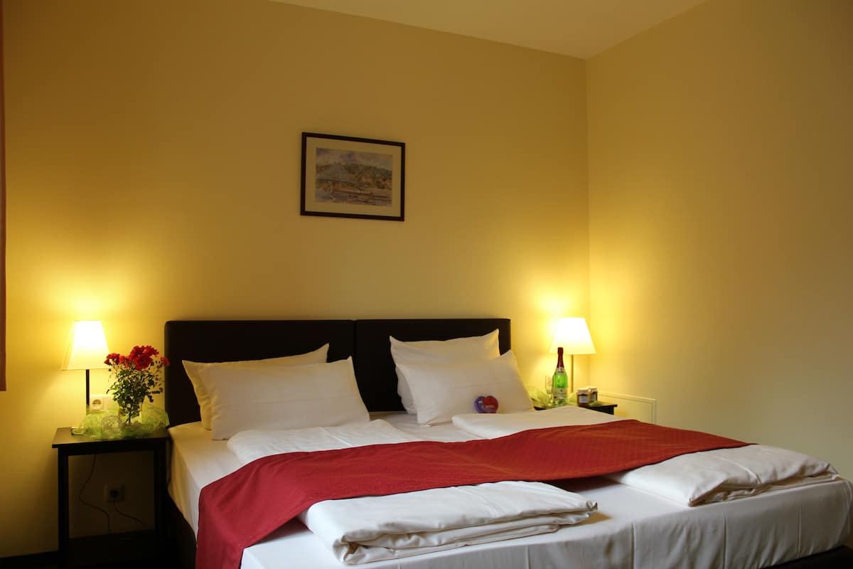 Une chambre d’hôtel avec un lit soigneusement fait, deux lampes de chevet, un tableau encadré au mur et une petite table sur laquelle est posé un vase de fleurs.