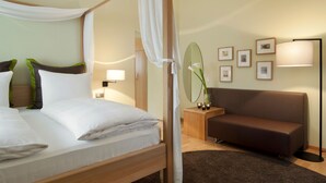 Une chambre d’hôtel avec un lit à baldaquin, un canapé, une table de chevet avec une lampe et des tableaux encadrés au mur.