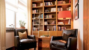 Un salon avec deux fauteuils en cuir, une bibliothèque en bois, un lampadaire rouge et une plante en pot.