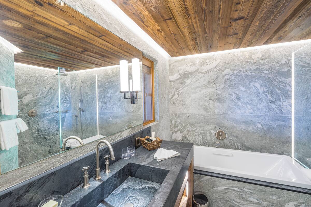 A bathroom with a marble sink, a large mirror, and a wooden ceiling.