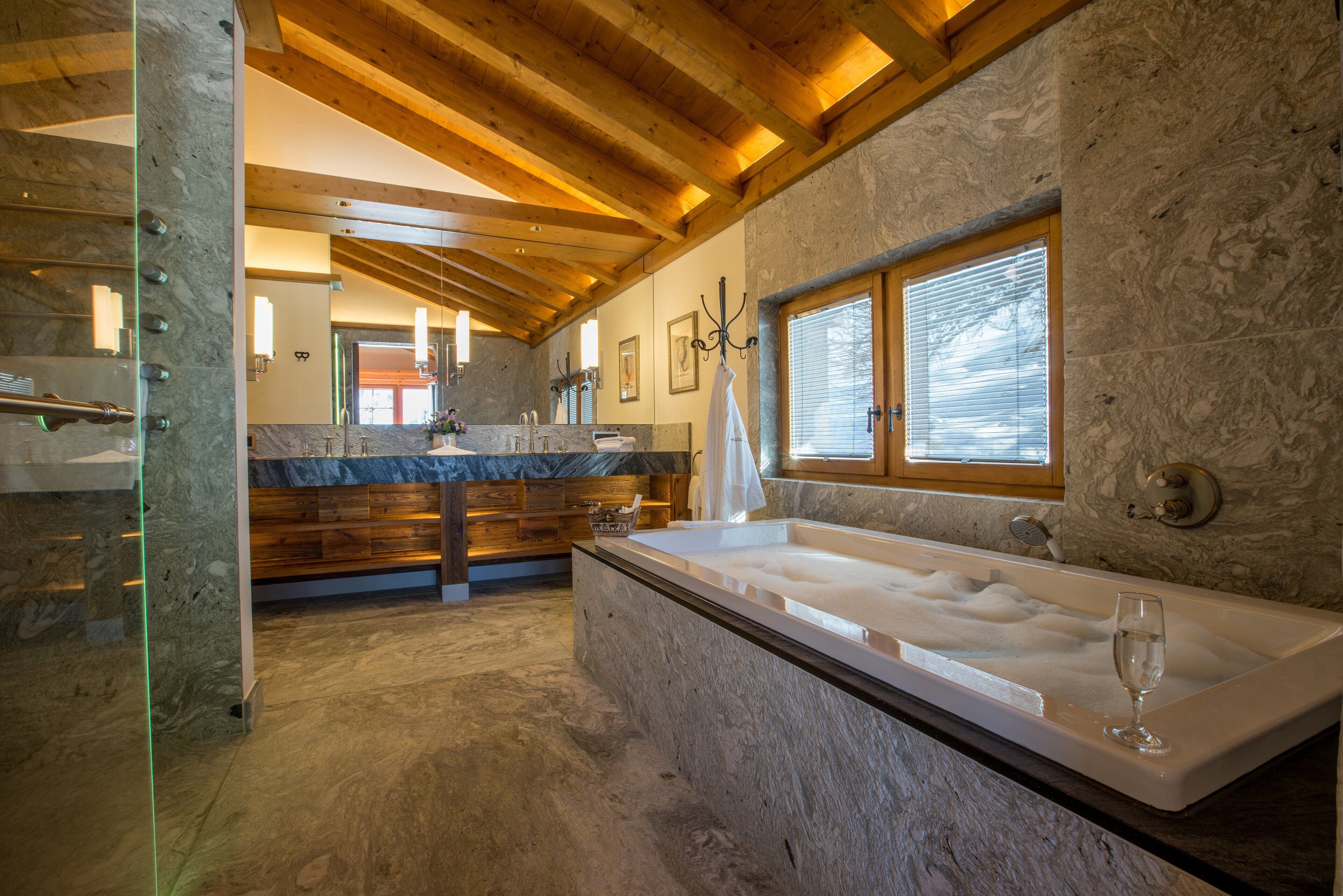 Une salle de bain avec une grande baignoire, des poutres en bois, des murs en pierre et une fenêtre.