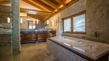 Une salle de bain avec une grande baignoire, des poutres en bois, des murs en pierre et une fenêtre.