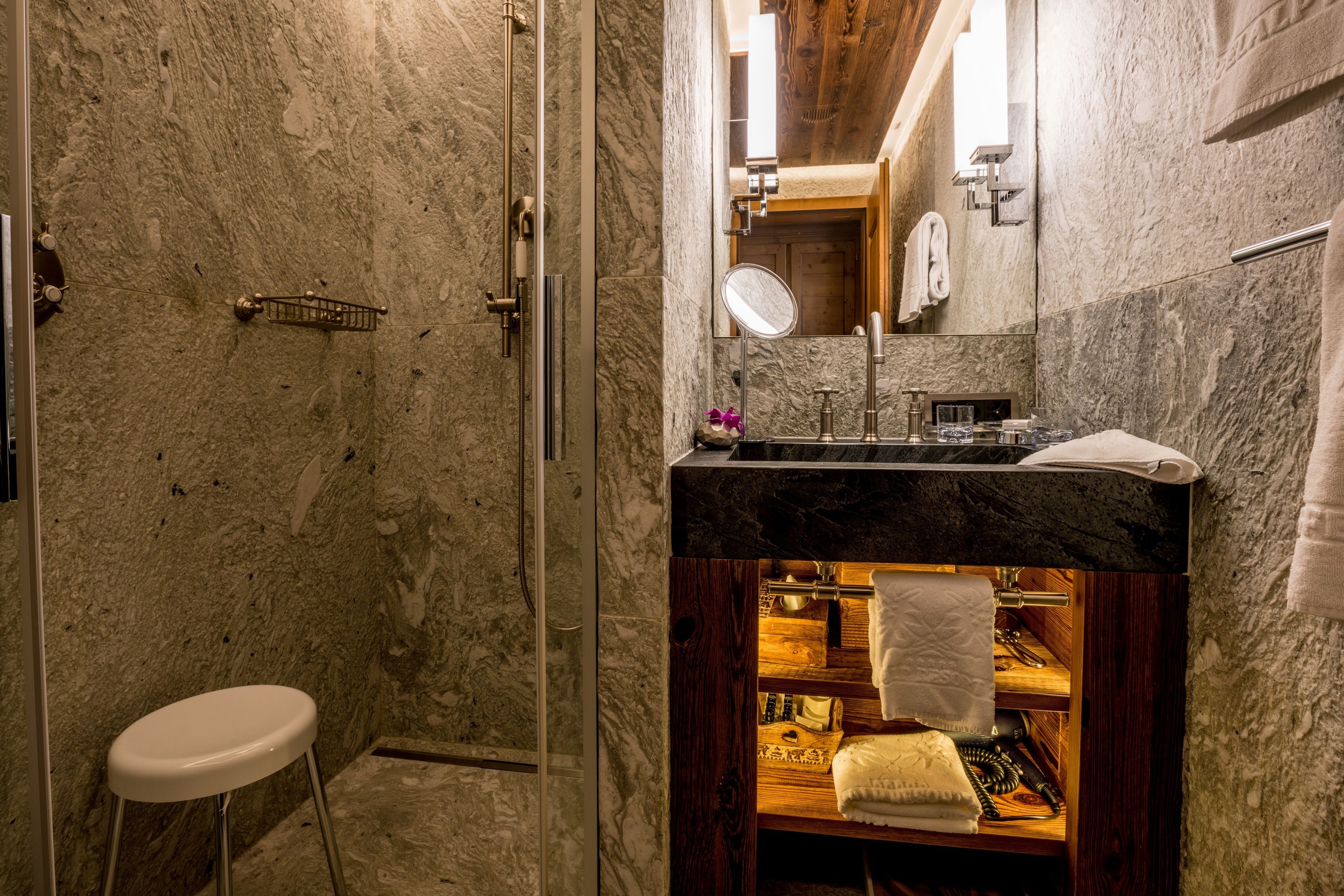 Une salle de bain avec un mur en marbre, un meuble-lavabo en bois, un miroir et des toilettes blanches.