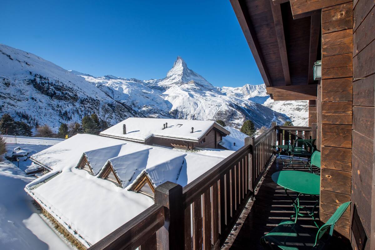 A wooden balcony with snow-covered roofs and a mountain view.